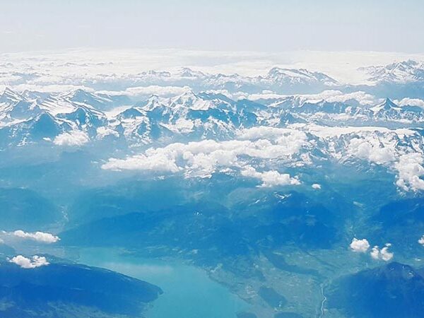 Aerial view of a mountain range with snow-capped peaks, clouds, and a lake nestled among the mountains.